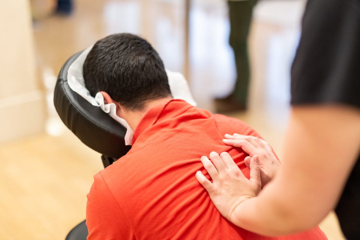 A therapist massaging the shoulders of a man seated in a massage chair